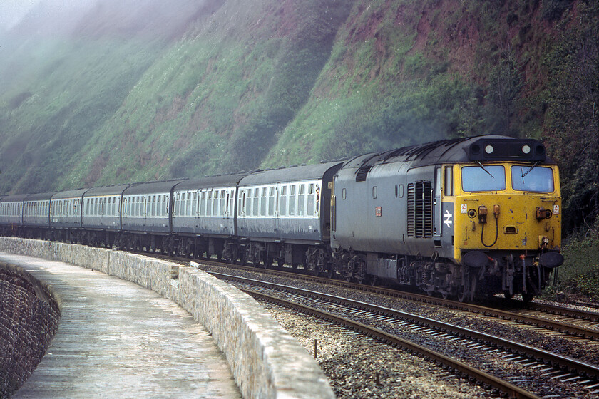 50042, 09.15 Penzance-Manchester Piccadilly, Parson's tunnel 
 A dramatic photograph taken using my 135mm telephoto lens attached to my Pentax ME Super shows 50042 'Triumph' approaching Parson's Tunnel on the South Devon sea wall leading the 09.15 Penzance to Manchester service. Unfortunately, by using the telephoto I have managed to crop out the rear of the train something that I also managed to achieve of a Class 50 hauled train at the same location two years previously, see..... https://www.ontheupfast.com/p/21936chg/26669851004/x50011-13-48-plymouth-london-paddington . 
 Keywords: 50042 09.15 Penzance-Manchester Piccadilly Parson's tunnel Triumph