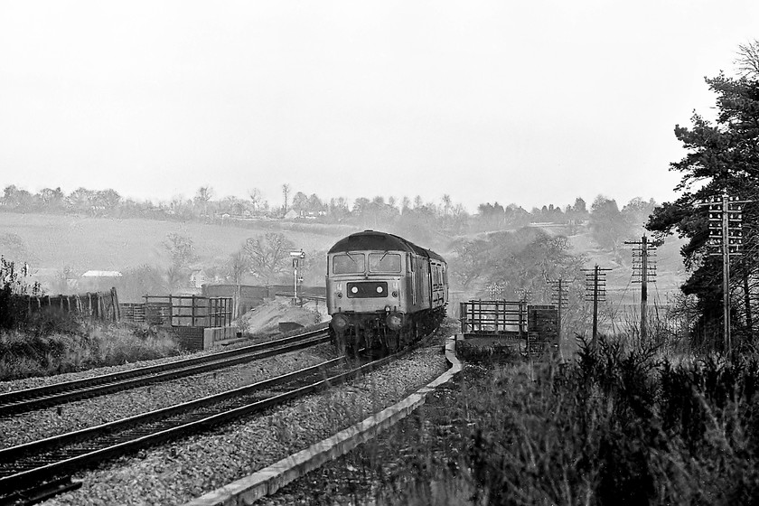 Class 47, unidentified down working, Lavington, ST996548 
 An unidentified Class 47 leads an afternoon down express past Lavington in Wiltshire. Just catching the last gasps of sunlight in the background is one of the up signals with a covered up colour light that would be switched on in exactly a week's time as Reading PSB took over control of this section of line. The picture is taken from the site of the old Lavington station (closed 18.06.66) with the locomotive crossing the bridge that has the A360 road underneath that is a favourite location for lorry strikes with a 4.6m (13' 6") clearance. 
 Keywords: Class 47 down working Lavington ST996548