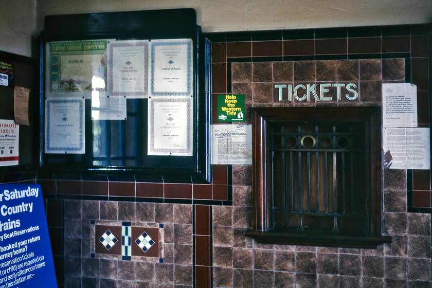 Booking hall, Tiverton Junction station 
 The booking office at Tiverton Junction station is seen complete with a number of best-kept station competition certificates in the wall-mounted cabinet. The art deco style tiling probably dates from the pre-war era when the station was re-modelled to speed up timings to the West Country. The station closed on 12.05.86 with the opening of Tiverton Parkway station some three miles northeast. It took another five years until the station was demolished, but I suspect that this lovely GWR tiling and other fittings were not saved. 
 Keywords: Booking hall Tiverton Junction station