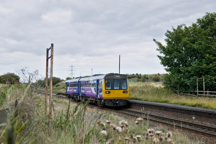 142084, NT12.45 Hexham-Nunthorpe (2N26), Greatham station (Closed 25.11.91) 
 Greatham station was opened by the Stockton and Hartlepool Railway in 1841 at a pretty remote and somewhat remote location some distance from the village it professed to serve. It was downgraded to an unmanned halt and survived the Beeching cull in large part due to the adjacent Cerebos salt factory many of whose workers used the station for commuting. Unfortunately, under BR traffic declined with a hopeless stopping pattern put in place that meant nobody was able to use the station with eventual closure by stealth coming on 24.11.1991. 142084 rattles through the remains of the station working the 12.45 Hexham to Nunthorpe service. 
 Keywords: 142084 12.45 Hexham-Nunthorpe 2N26 Greatham station Closed 25.11.91 Northern Trains Pacer