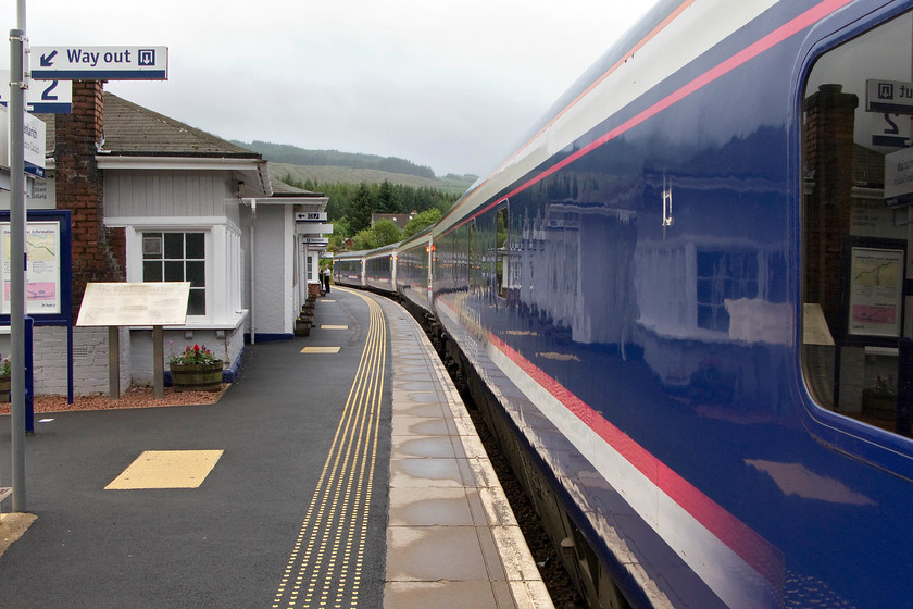 Stock, CS 21.16 London Euston-Inverness, Fort-William & Aberdeen sleeper (1S25 & 1Y11), Crianlarich station 
 Looking back along the platform at Crianlarich station sees the Mk. III sleeper stock of the Fort William portion of the down Highland Sleeper service pausing to wait for the passage of a train going in the opposite direction towards Glasgow. Notice that all the stock in this view has yet to receive Caledonian Sleeper's teal livery with the stock still wearing the former ScotRail blue. Along with the rest of the stations on the Highland Line Crianlarich was very smart and well-maintained. 
 Keywords: Stock 21.16 London Euston-Inverness, Fort-William Aberdeen sleeper 1S25 1Y11 Crianlarich station Caledonian sleeper Mk. III