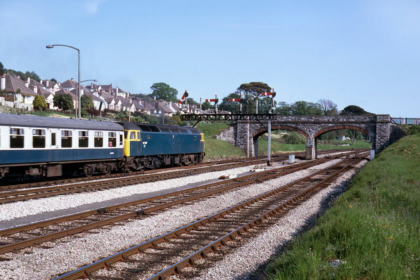 47467, 09.08 Newcastle-Paignton, Aller Junction 
 The 09.08 Newcastle to Paignton service approaches the end of its journey, seen at Aller Junction. 47467 is about to lead the train under the superb four doll gantry along with two unused dolls. The gantry was installed in 1962 following the simplification of the junction with the consequential removal of a pair of matching three doll brackets that themselves were installed in 1941 during wartime alterations. What really strikes one in this photograph is the neatness of the embankments and the trackbed. The bullhead track is laid on immaculate ballast with no weeds and looks almost manicured! The network is not maintained like this today with rampant and uncontrolled growth encroaching and creating its own problems, particularly during the leaf fall season. 
 Keywords: 47467 09.08 Newcastle-Paignton Aller Junction