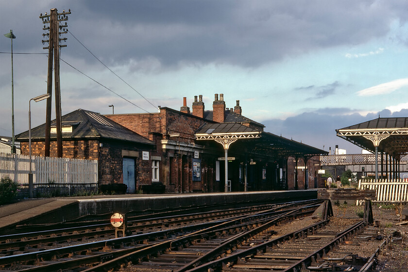 Melton Mowbray station 
 The history of stations and their various names over the years in Melton Mowbray would warrant a small essay in itself! By 1981, when this photograph was taken, this original 1846 station was opened by the Midland Counties Railway and was the only station in the town. It was designed by William Parsons and Sancton Wood but for once, they did not quite go far enough in their work with a large porte-cochre later added to the frontage as a result of competition from the Great Northern and London and North Western Joint Railway which opened its station, Melton Mowbray North, in 1879. This evening scene shows the station with all of its infrastructure appearing to be in need of a little loving care and attention! 
 Keywords: Melton Mowbray station