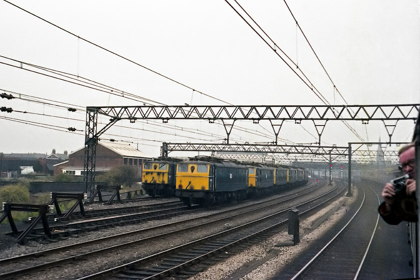 76014, 76004, 76041, 76001, 76051, 76040, 76047 & 76054, stabled, Guide Bridge 
 As we speed past Guide Bridge yard a line-up of stabled class 76s are on view. They are 76014, 76004, 76041, 76001, 76051, 76040, 76047 and 76054. Behind the spotter with his camera, that looks to be an Olympus Trip, is the spire of St. Stephens church located at the junction of Stockport Road and Guide Lane in the district of Audenshaw. 
 Keywords: 76041 76001 76051 76040 76047 76054 Guide Bridge