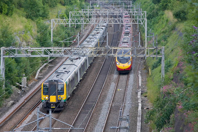 350242 & 350120, LM 18.13 London Euston-Birmingham New Street (1Y69) & 390032, VT 18.20 London Euston-Manchester Picadilly (1H02), Roade cutting 
 The timing is not quite spot-on for the perfect framing of the two trains in view as they pass through Roade cutting. 350242 and 350120 are partially obscured by the wiring as they work the 18.13 Euston to Birmingham London Midland service. However, 390120 is just a few metres too far back partially obscured by the stanchion as it works Virgin's 18.20 Euston to Manchester service. Better luck next time! 
 Keywords: 350242 350120 18.13 London Euston-Birmingham New Street 1Y69 390032 18.20 London Euston-Manchester Picadilly 1H02 Roade cutting London MIldand Desiro Virgin Pendolino