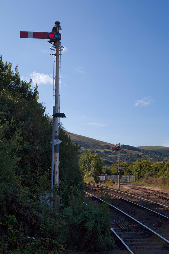 Starter signals, Girvan station 
 For anybody who takes Traction magazine, a bi-monthly publication for which I produce occasional articles, they will have seen an almost identical picture to this image on page 11 of edition 247 (September/October 2018). Admittedly, my shot does not have a pair of 40s and some Mk1 stock but the semaphores are the same but with a bit more lineside vegetation! In this view, looking south, the hills in the distance are those to be surmounted on immediately leaving the station. This involves some three miles 1:54 climbing to Pinmore Tunnel, then, following a decent, a sustained nine miles of climbing through Barrhill to milepost 16. 
 Keywords: Starter signals Girvan station