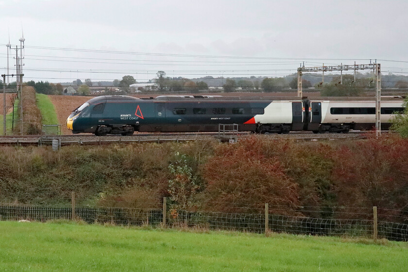 390154, VT 15.16 London Euston-Glasgow Central (9S85, 1L), Roade hill 
 From the bright sunshine of the morning, the cloud has come in and makes for a dull and grey afternoon. 390154 passes between Roade and Ashton in Northamptonshire working the 9S96 15.16 Euston to Glasgow Central. Notice two of the M1 windfarm turbines to the extreme left, a familiar sight to those who pass them on the busy M1 motorway on the other side from this view. 
 Keywords: 390154 15.16 London Euston-Glasgow Central 9S85 Roade Hill Avanti West Coast Pendolino