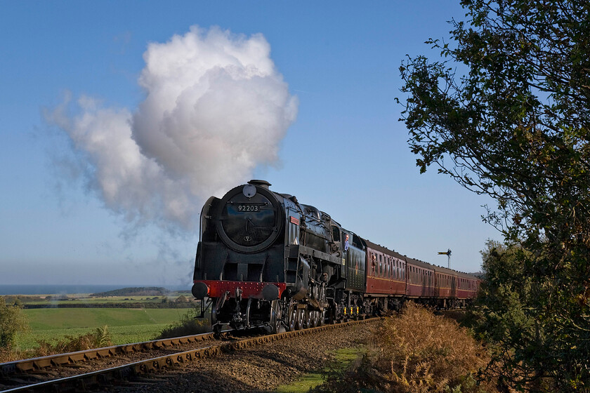 92203, 10.30 Sheringham-Holt, Kelling bank 
 Sometimes things just come together but in railway photography, this is the exception rather than the rule! In intense bright autumn sunshine 92203 'Black Prince' ascends Kelling bank between Weybourne and Holt working the North Norfolk Railway's 10.30 Sheringham to Holt service. The inclusion of the sea, to the detriment of having the entire train in view, and the driver leaning from the cab adds to the scene but the only issue for me is that the sun has not quite come around far enough to fully illuminate the front of the 9F. 
 Keywords: 92203 10.30 Sheringham-Holt Kelling bank Black Prince 9F