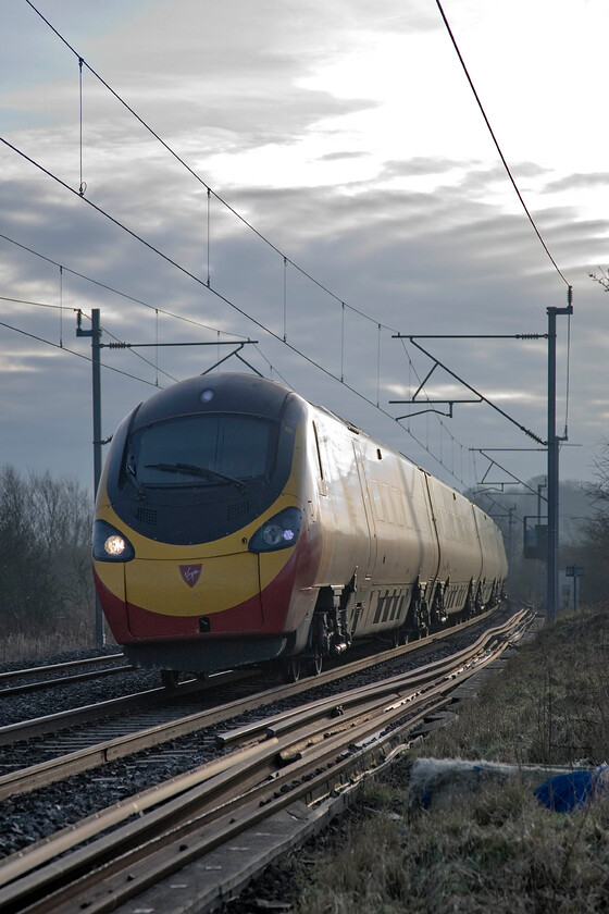 Class 390, VT 07.30 London Euston-Glasgow Central, Bugbrooke SPO676565 
 Breaking all the rules by taking into the rising sunshine, thankfully tempered by some low cloud, a Class 390 Pendolino passes near the Northamptonshire village of Bugbrooke with the 07.30 Euston to Glasgow Central service. This service is the first down Anglo-Scottish express of the day. 
 Keywords: Class 390 07.30 London Euston-Glasgow Central Bugbrooke SPO676565 Virgin West Coast Pendolino