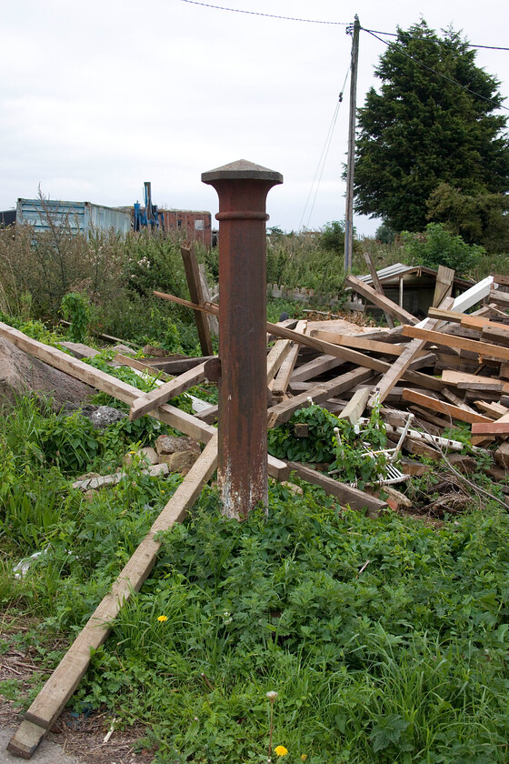 Gate post, Murrow West 
 This lone cast iron gate post looks lost amongst the uncut grass and general detritus at Murrow West. I suspect that it was once associated with the station that closed on 06.07.53 as it was located directly behind it close to the trees and the old containers. The group of lads who turned up to sort through the wood did not seem to understand why I was taking a photograph of this post and I did not explain as I suspect that it would be lost on them! 
 Keywords: Gate post Murrow West