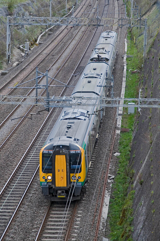 350116, LM 11.46 London Euston-Crewe, Roade cutting 
 Running on the down fast line through Roade cutting 350116 is seen working the 11.46 Euston to Crewe train. These services run 'fast' as far as Rugby and then become, effectively, all station stopper services beyond via Nuneaton and Stafford or Stoke. 
 Keywords: 350116 11.46 London Euston-Crewe Roade cutting London Midland Desiro