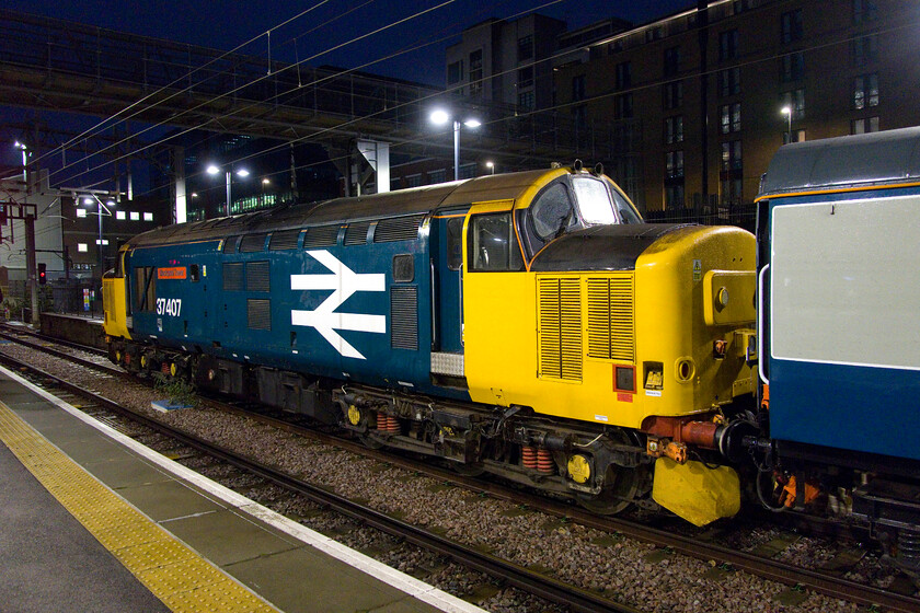 37407, outward leg of the Carols at Norwich Cathedral, 07.22 London King's Cross-Norwich (1Z39, RT), London King's Cross station 
 Looking superb in its large logo livery 37407 'Blackpool Tower' stands idle at the rear of the ECS of the Carols at Norwich Cathedral charter at a dark King's Cross. Within a few minutes, it should be started up and ready to depart at 07.22. Unfortunately, due to its late inbound arrival, this did not happen with it eventually leaving about fifteen minutes late. I have seen and photographed this Class 37 a number of times most notably when it was hired in by Greater Anglia in 2018, ironically on tracks that it would be re-visiting later on this day, see... https://www.ontheupfast.com/p/21936chg/23911824404/x37407-37405-2j80-cantley-station 
 Keywords: 37407 Carols at Norwich Cathedral 07.22 London King's Cross-Norwich 1Z39 London King's Cross station Blackpool Tower