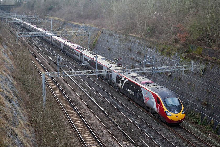 390104, VT 12.57 London Euston-Manchester Piccadilly (1H10, 1E), Roade Cutting 
 350104 'Alstom Pendolino' heads north through Roade Cutting forming the 12.57 Euston to Manchester Piccadilly. This 11-car Pendolino has a unique branding with two sets of vinyls to commemorate the 175th anniversary of Longsight Depot and the other to recognise the working relationship between Virgin and Alstom. 
 Keywords: 390104 12.57 London Euston-Manchester Piccadilly 1H10 Roade Cutting