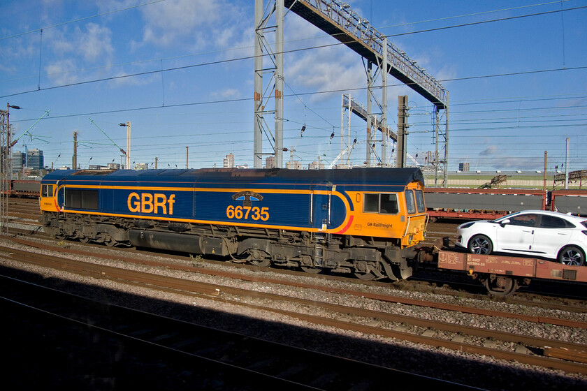 66735, 09.28 Dagenham Docks-Gaston (6X43, 20E), Wembley Yard 
 66735 'Peterborough United' is seen held in Wembley Yard leading the 6X43 09.28 Dagenham Docks to Garston car transporter train. The train contained a good representative example of Ford's car and van range all built in mainland Europe and imported to the UK. They are transported by rail to Garston for distribution around the country by the car giant. Of course, the likelihood is that many of the vehicles will have been fitted with engines that were built at Dagenham and then themselves sent across the channel to be installed into the cars being built abroad; I suppose it makes sense to someone! 
 Keywords: 66735 09.28 Dagenham Docks-Gaston 6X43 Wembley Yard Peterborough United Ford