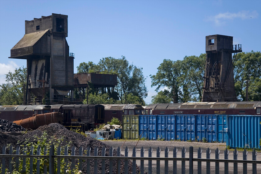 Coaling stages, Carnforth WCR 
 Both the taller mechanical coaling stage and the smaller ash plant at Carnforth are Grade II listed structures by Historic England. In their citation Historic England waxes lyrical about the efforts to which the LMS went to in order to drive efficiency in the Steam Age and that these probably represented the pinnacle of their efforts. Another factor that led to their designation is that they both still contain the operational mechanicals that were, thankfully, not stripped out when steam finished at the depot in 1968. Notice the lineup of various locomotives in the foreground, some in working order, others not and to be used for spares. 
 Keywords: Coaling stage & ash plant, Carnforth WCR