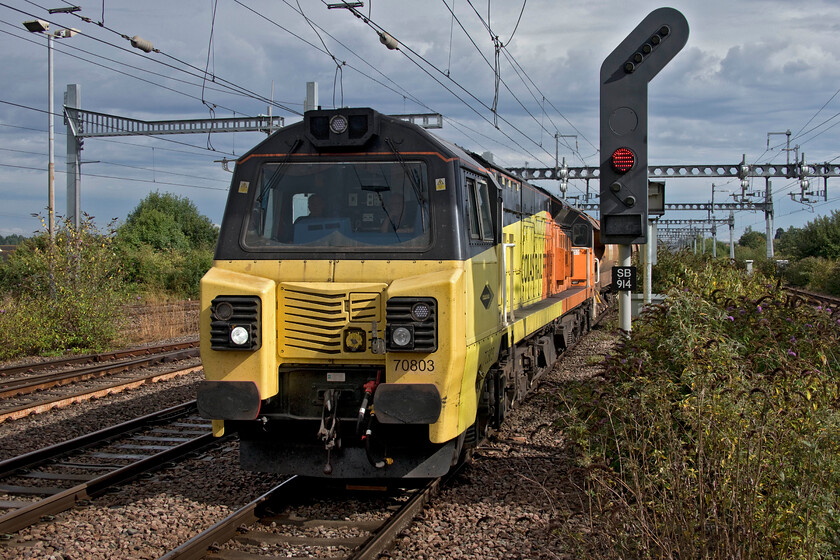 70803, 13.27 Eastleigh East Yard-Hinksey Yard (6X27, 3L), Didcot Parkway station 
 With the rain having passed over and the sun out again 70803 drifts slowly into Didcot Parkway station leading the 6X27 13.27 Eastleigh East Yard to Hinksey Yard infrastructure train. The train crept to a halt with a very unhurried crew change taking place. Looking at this image and one taken slightly further along the platform half an hour earlier (https://www.ontheupfast.com/p/21936chg/30031743883/x387149-387167-13-27-london-paddington) the difference that a bit of sun makes is remarkable! 
 Keywords: 70803, 13.27 Eastleigh East Yard-Hinksey Yard (6X27, 3L), Didcot Parkway station. Colas