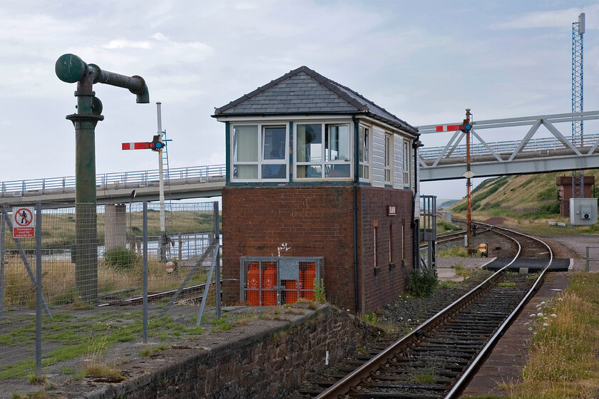 Sellafield signal box (Furness, 1918) 
 With both the trains seen in the previous photographs having departed all has gone quiet at Sellafield and the signalman has returned to his seat having completed the train register. Apart from passenger workings every hour or so the other work that the signalman has is when a flask train arrives or departs from the adjacent reprocessing plant. The box at Sellafield was built by the Furness Railway in 1918. Whilst it's a functional affair it does look a little odd without its chimney stack. The surviving water column on the platform end is an interesting survivor. It was supplied by water from the large stone-built water tower seen to the extreme right beyond the bridge. 
 Keywords: Sellafield signal box Furness 1918