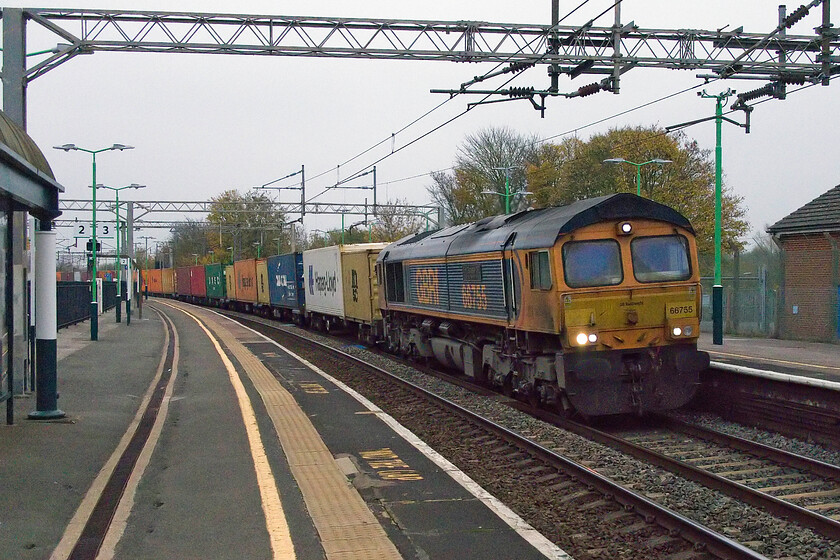 66755, 06.21 Hams Hall-London Gateway (4L12, 17E), Wolverton station 
 In appalling light, 66755 'Tony Berkeley OBE RFG Chairman 1997-2018' passes through Wolverton at speed leading the 4L12 06.21 Hams Hall to London Gateway GBRf service. This image has needed a fair amount of work to make it presentable but, even so, it is far from the best quality with considerable digital noise. 
 Keywords: 66755 06.21 Hams Hall-London Gateway 4L12 Wolverton station Tony Berkeley OBE RFG Chairman 1997-2018 GBRf