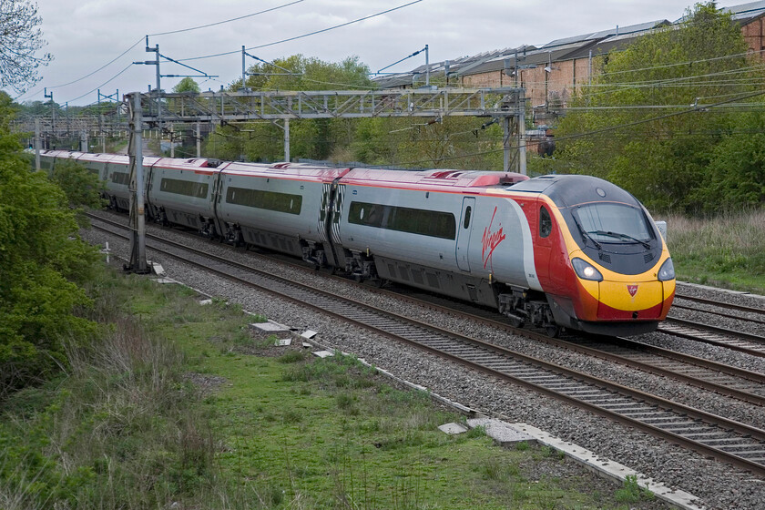 390043, VT 13.40 Glasgow Central-London Euston, Roade 
 Seen from the western side of the WCML in Roade 390043 'Virgin Explorer' works the 13.40 Glasgow Central to Euston. From this side of the line, the former Pianoforte factory site can be clearly seen behind the train. With the factory finally closing a few years ago its future is uncertain with a plan now on the table to demolish the whole site and build a new housing estate. 
 Keywords: 390043 13.40 Glasgow Central-London Euston Roade Virgin Trains Virgin Explorer