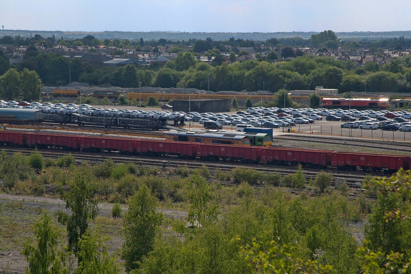 66733, 66004, Toton centre road 
 Taken from Toton's infamous 'bank' looking southwest this scene is dominated by Toyota's recently opened export distribution hub. Notice the train to the left in the process of being loaded with cars that would then work south via the MML (as 6X11) to Dollands Moor and thence through the tunnel to Europe. In the foreground 66733 'Cambridge PSB' sits at the front of a short infrastructure working with Climate Hero liveried 66004 tucked in behind. In the very background to the right is a DB liveried Class 66 stored with long-term resident Class 60 just in view. Notice in the very top left hand corner the air traffic control tower of East Midlands Airport. 
 Keywords: 66733 Cambridge PSB 66004 Toton centre road