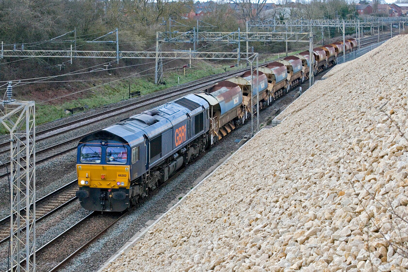 66302, 14.16 Bescot Yard-Tring (6G65, RT), Ashton Road bridge 
 It is a little unusual to see an engineering train such as this, the 14.16 Bescot Yard to Tring 6G65 on a Thursday normally seeing them at the weekend. However, with engineering work planned this weekend coming it looks like Network Rail is getting themselves ready by getting the ballast close to the work site lead on this occasion by former DRS 66302. Passing just south of Roade the relatively short train took a slightly out-of-the-way route heading all the way south to Wembley Yard to then retrace its steps to Tring arriving much later in the evening. 
 Keywords: 66302 14.16 Bescot Yard-Tring 6G65 Ashton Road bridge