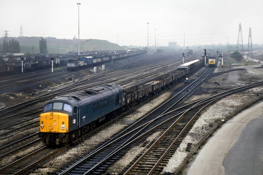 44007, down freight, Toton Yard 
 After I saw the two class 44s from the lofty height of the Toton bank, I dashed as quickly as I could back to the A52 bridge and got there just as 44007 was pulling away with its PW train. I grabbed a shot in the gathering gloom. 44007 (ex D7 'Ingleborough') survived, along with all the remaining three Class 44s, in-service for just over a year until 30.11.80 when all were withdrawn. As it was still serviceable, 44007 undertook its final journey under its own power to Derby works were it was broken up within a year. 47355 is seen held at a signal awaiting access to the depot and fueling point. It will draw forward and then reverse into the depot on one of the lines curving off to the right. 
 Keywords: 44007 freight Toton Yard