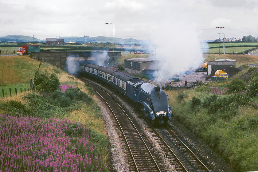 4498, outward leg of The Cumbrian Coast Express, 10.23 Blackpool North-Sellafield, Lindal SD262764 
 With the outward leg of The Cumbrian Coast Express having a thirty minute stop at Grange-over-Sands, we had an opportunity to get it further west. We all piled back into the Mini and raced from Grange to Lindal situated between Ulverston and Dalton-in-Furness. This was a fair distance on some roads that take pretty indirect routes due to the estuaries and, also, the A590 was not dual carriageway then, as large sections are today, so we must have done pretty well! We arrived just in time to see 4498 'Sir Nigel Gresley' bringing the train up Lindal Bank with a bit more exhaust than when it was seen earlier. The picture is taken from a minor road with a Ford D series truck crossing the new replacement bridge in the background. 
 Keywords: 4498 The Cumbrian Coast Express 10.23 Blackpool North-Sellafield Lindal SD262764