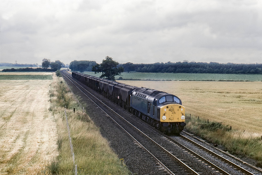 40050, down grain hoppers, Naburn SE608445 
 This is a simple but fascinating picture for a number of reasons. A down working composed of forty-one ton covered grain hopper wagons is seen passing Naburn south of York hauled by 40050. This four axle PAA wagons date from the early 1970s and were designed to carry considerable amounts of malt and grain around the country in trains that became part of the Speedlink network. Apart from the trackbed and Naburn Wood in the background, everything in this scene has gone. The class 40 survived for exactly another four years before withdrawal. The hoppers will have long been disposed of, but some survived into the late 1980s, and the line itself is now a footpath and cycleway. This former section of the ECML that ran from just north of Selby to Challoners Whin Junction was closed in 1983 following the opening of the Selby Diversion, a thirteen-mile section of new track. 
 Keywords: 40050 grain hoppers Naburn SE608445