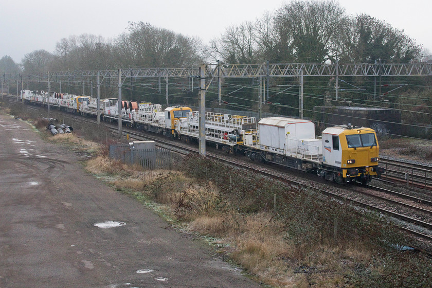 DR98009, DR98011, DR98004 & DR98003, 11.27 Chelmsford reception-Crewe TMD (6YXX, 33E), site of Roade station 
 A cavalcade of track machines passes Roade made up of four Windhoff overhead line electrification MPVs. Working as the 11.27 Chelmsford to Crewe DR98009 'Melvyn Smith', DR98011, DR98004 'Phillip Cattrell' and DR98003 pass along the down slow line. After a bright, cold and frosty start to the day by this time, later in the afternoon, the fog had come down and it had turned bitter! 
 Keywords: DR98009 Melvyn Smith DR98011 DR98004 Phillip Cattrell & DR98003, 11.27 Chelmsford reception-Crewe TMD (6YXX, 33E), site of Roade station