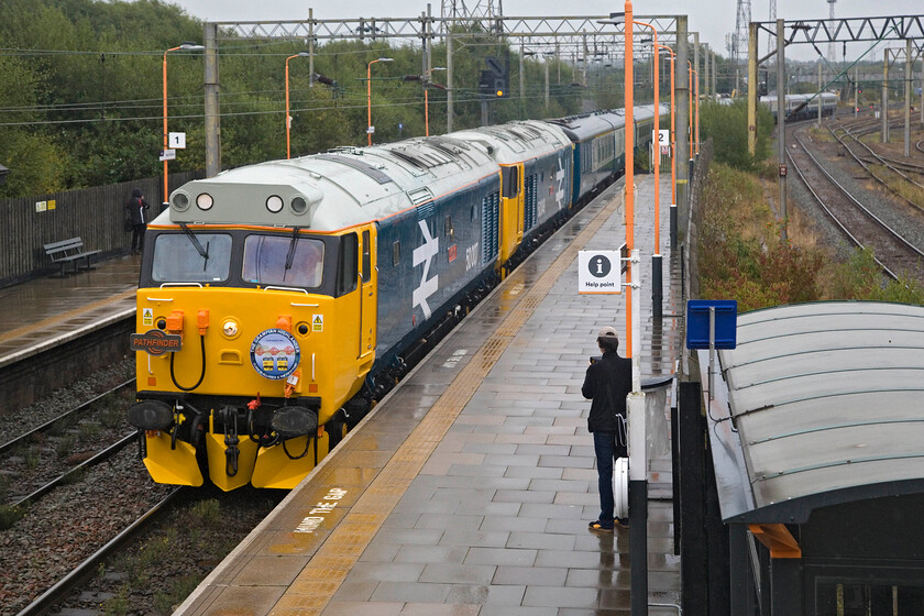 50007 & 50049, outward leg of The Grampian Highlander (Day 1), 06.05 Taunton-Aberdeen (1Z72, 5L), Bescot Stadium station 
 Despite the heavy rain and general dullness was it worth it? Yes it was! The sight of a pair of matching large logo Class 50s certainly brightens up the morning as they make their way through Bescot Stadium station. They are leading the outward leg of Pathfinder's epic three-day Grampian Highlander charter. The appearance of 50007 'Hercules' leading 50049 'Defiance' certainly attracted the attention of many local enthusiasts with the station busy with about ten in various spots, trying to get their shot including a chap to my immediate right trying to protect his very expensive-looking video equipment from the rain! The charter was a resounding success over the three days with this leg, that left Taunton at 06.05, arriving just five minutes late in the Granite City. 
 Keywords: 50007 50049 The Grampian Highlander Day 1 06.05 Taunton-Aberdeen 1Z72 Bescot Stadium station Hercules Defiance