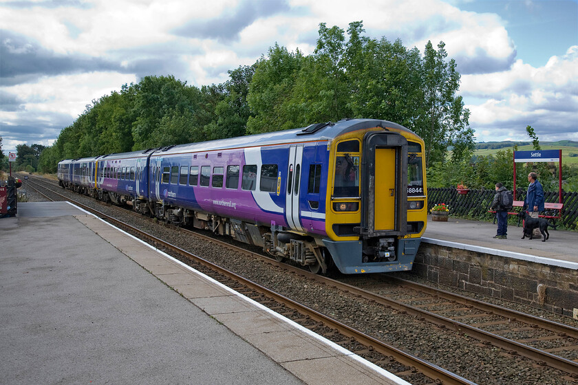 158844 & 158877, NT 10.49 Leeds-Carlisle (2H86), Settle station 
 During the busy summer months services that traverse the Settle and Carlisle route are usually strengthened to two-car sets. Here at Settle station 158844 and 158877 arrive working the 2H86 10.49 Leeds to Carlisle service. The photograph does not reveal the many passengers waiting to board the train ready to enjoy a journey over one of the most dramatic railway lines in the country. 
 Keywords: 158844 158877 10.49 Leeds-Carlisle 2H86 Settle station Northern