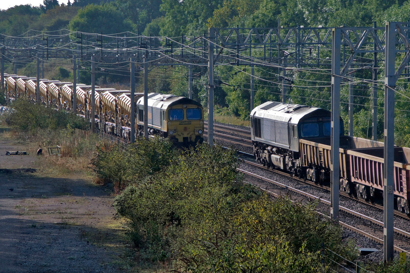 66546, switched off, HOBC train & Class 66, ballast train, site of Roade station 
 66546 to the left is seen at Roade where the former station used to be located. It is switched off at the head (or tail) of an HOBC (drain) train. To the right unidentified Class 66 is also stationary but with its engine running on the down slow line. It is attached to a rake of IOA open ballast wagons 
 Keywords: 66546 HOBC train Class 66. ballast train site of Roade station