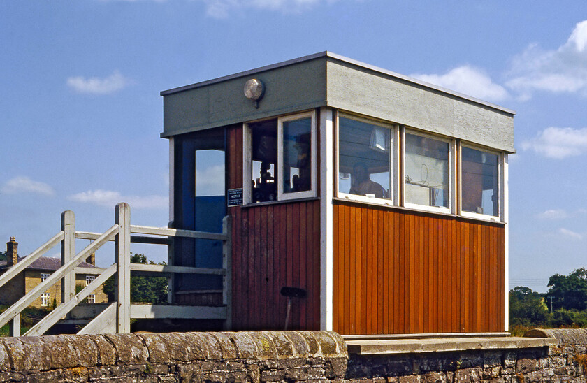 Onibury signal box (BR, 1977) 
 An unusual design, Onibury signal box was just three years old when this photograph was taken. This 1977 BR structure, sitting in a semi-elevated position on a concrete slab staddling a stone wall, replaced a traditional LNW & GW joint box located on the opposite side of the tracks and the northern side of the A49 level crossing. This view shows the rear of the box taken from a field but I did manage a semi-front view during my most recent visit in 2016, see....https://www.ontheupfast.com/p/21936chg/25752986404/onibury-signal-box 
 Keywords: Onibury signal box BR 1977