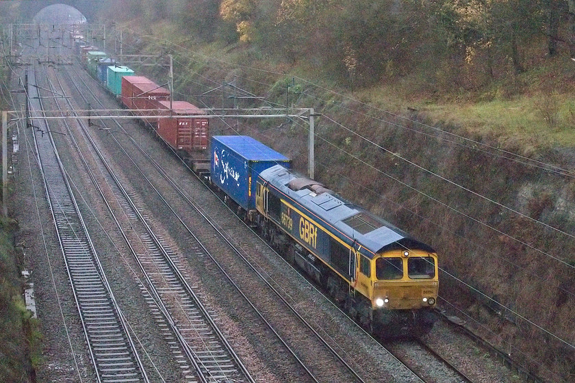 66739, 13.00 Hams Hall-Wembley Reception sidings (4L21, 3L), Hyde Road bridge 
 66739 'Bluebell Railway' heads slowly through Roade cutting taken from Hyde Road bridge in the village of the same name leading the 13.00 Hams Hall to Wembley Freightliner service. The weather was absolutely foul by this time with torrential rain and appalling light that required the camera to operate at 20000 ISO! I have included this photograph of what is, after all, a pretty ordinary working on my home patch as a credit to my dogged perseverance in awful weather! 
 Keywords: 66739 13.00 Hams Hall-Wembley Reception sidings 4L21 Hyde Road bridge Freightliner Bluebell Railway