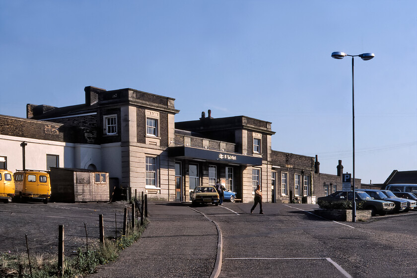 Frontage, Ely station 
 The first station at Ely was opened by the Eastern Counties Railway in 1844 changing little by 1981, when this photograph was taken, and indeed today for that matter. It was slightly more ornate and included some towers that were removed by the LNER when they rebuilt the station in 1929-1930. The original structure was modelled by Francis Thompson (not Sancton Wood as may would have you believe) and is now Grade II listed. I suspect that the station will have outlived the various cars in the station car park on this warm summer evening including a rather nice yellow Mk.II Vauxhall Cavalier. 
 Keywords: Frontage Ely station