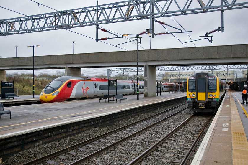 390002, VT 07.55 Manchester Piccadilly-London Euston (1R28) & 350254, 350238 & 350255, LM 08.24 London Euston-Milton Keynes (2K21), Milton Keynes station 
 Milton Keynes station is a pretty soulless station in the best modernist style of the 1970s. Designed by the MKDC's (Milton Keynes Development Corporation) architect Stuart MosscropIt the station was opened in 1982 after much procrastination, largely from cash strapped BR. They maintained that their InterCity offer to and from Bletchley was perfectly adequate in terms of serving nearby Milton Keynes. In this grey February view 390002 pauses working the 07.55 Manchester to Euston service whilst 350254, 350238 and 350255 have just terminated with the 08.24 from Euston. 
 Keywords: 390002 07.55 Manchester Piccadilly-London Euston 1R28 350254 350238 350255 08.24 London Euston-Milton Keynes 2K21 Milton Keynes station