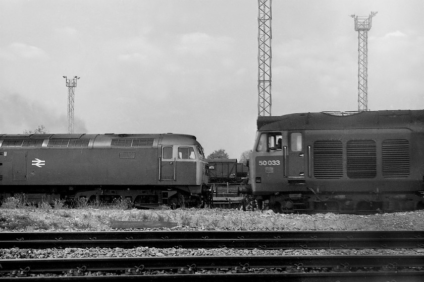 50033, down Foster Yeoman empty stone working & 47144, unidentified up working, Westbury South 
 An interesting picture taken at Westbury South. It shows to the left, a Cardiff Canton based 47144 bringing an unidentified up working into Westbury slowing for its stop at the station about a mile away. To the right, 50033 'Glorious' is getting an empty Foster Yeoman stone wagon train under way after a brief stop at Westbury. This will be heading from the London area to one of the Mendip quarries. The two tracks in the foreground are the up and down Salisbury lines that diverge from the other two lines at Westbury South. 
 Keywords: 50033 Foster Yeoman empty stone 47144 Westbury South